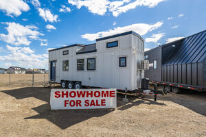 A tiny home exterior with white siding, black accents and a blue door