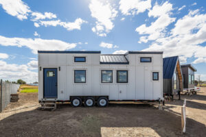 A tiny home exterior with white siding, black accents and a blue door