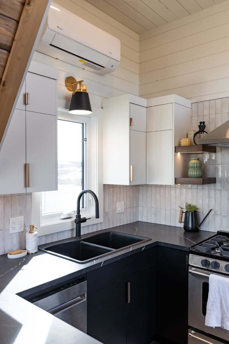 Tiny home kitchen with black marble counter tops, white cabinets, black sink, white tile backsplash, and modern stove