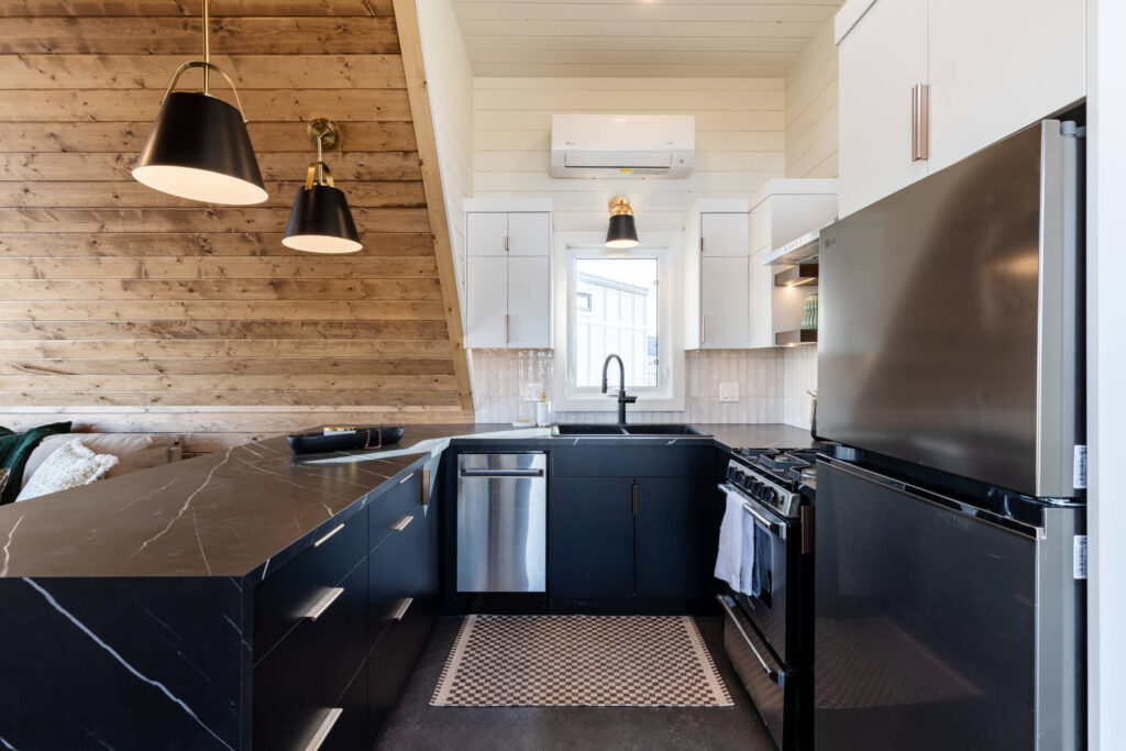 Tiny home kitchen with black marble counter tops, white cabinets, black sink, and wood accents