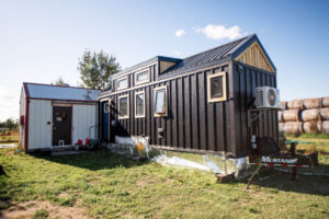 Modern black tiny house exterior with metal roof and multiple windows on trailer foundation
