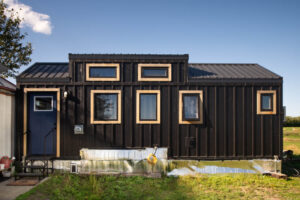 Front exterior of modern black tiny home with wood window trim and compact entry stairs