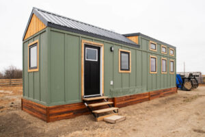 Green tiny house exterior with black door, wood trim, metal roof and steps leading to the entrance.