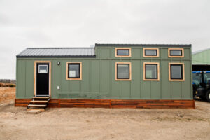 Side view of modern tiny house with green siding, wood trim windows and metal roof.