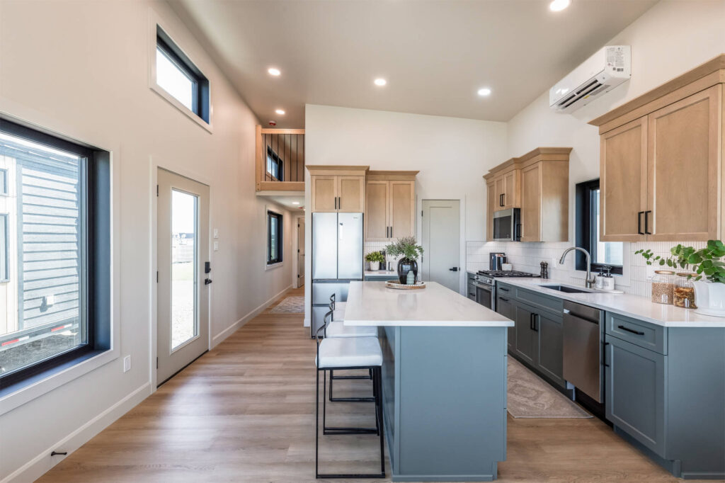 Tiny home open kitchen with light wood and blue cabinets, white countertops and an island