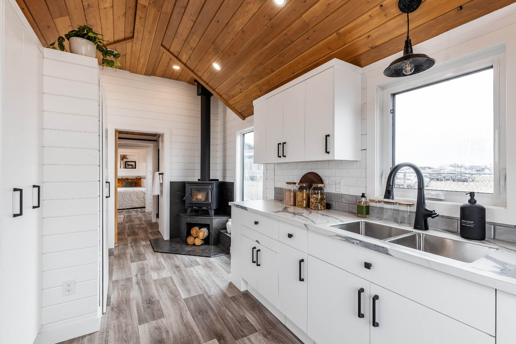 A spacious kitchen with white cabinets in a tiny home, featuring a cozy wood stove.