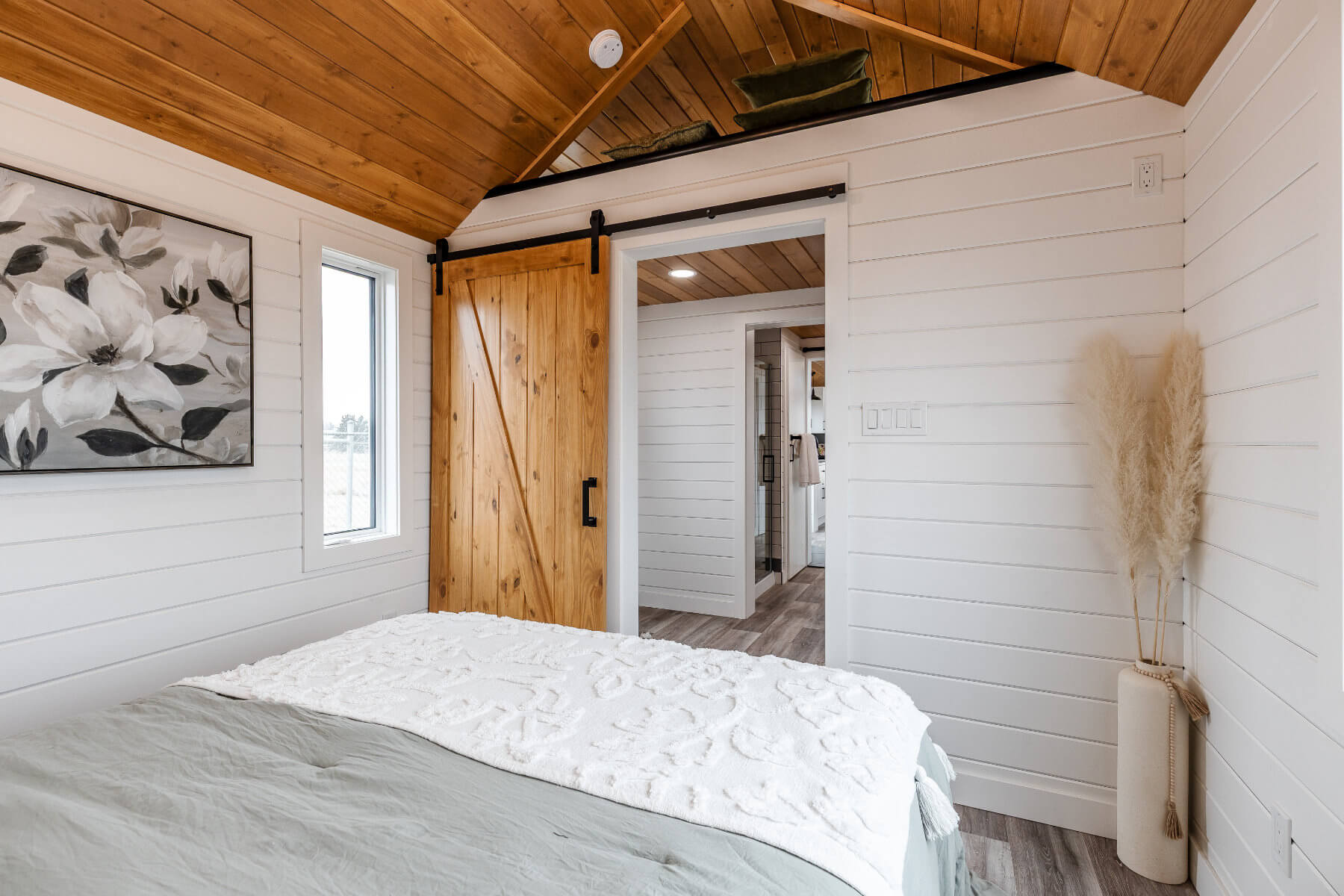 A specious and bright tiny home bedroom with white walls and a rustic barn door